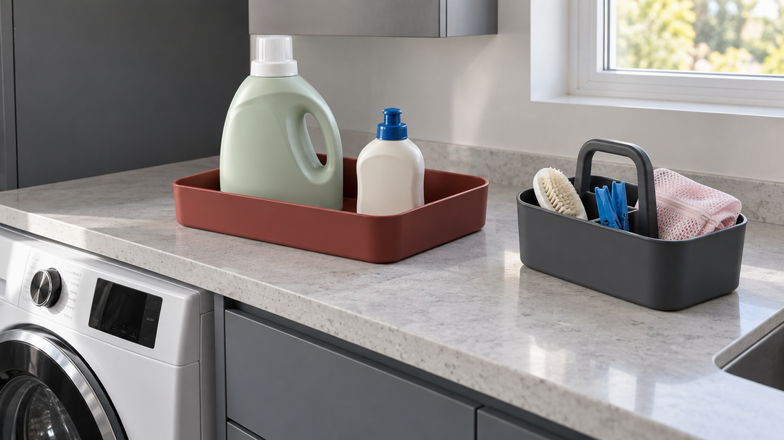 Brick-red tray holding laundry bottles beside a charcoal handled caddy with a scrub brush, blue clothespins, and a pink mesh wash bag.