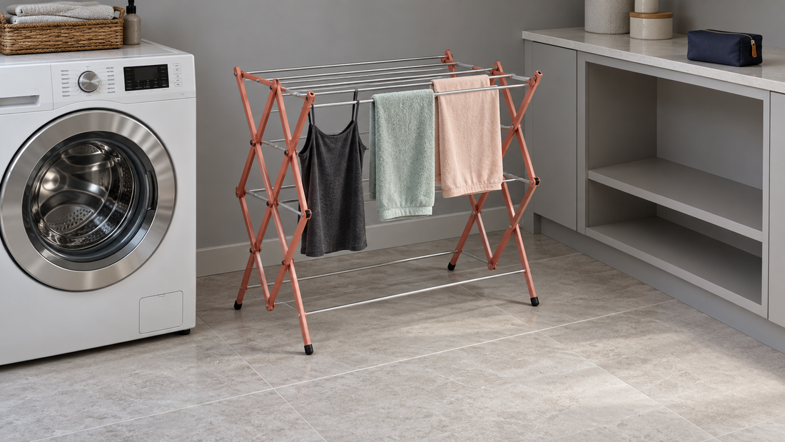 An open coral accordion drying rack holds laundry beside a white washer, with clear floor space in front and empty cabinet shelves nearby.