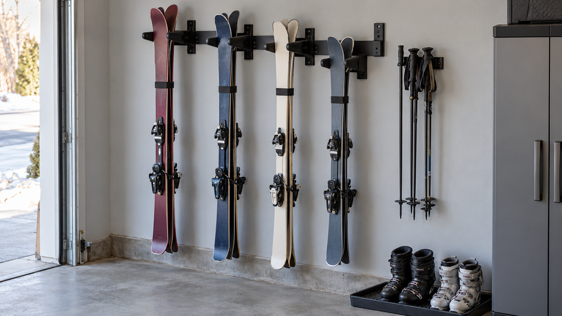 Four pairs of skis hang in separate holders on a garage wall rack, with ski poles stored alongside and the floor clear below.