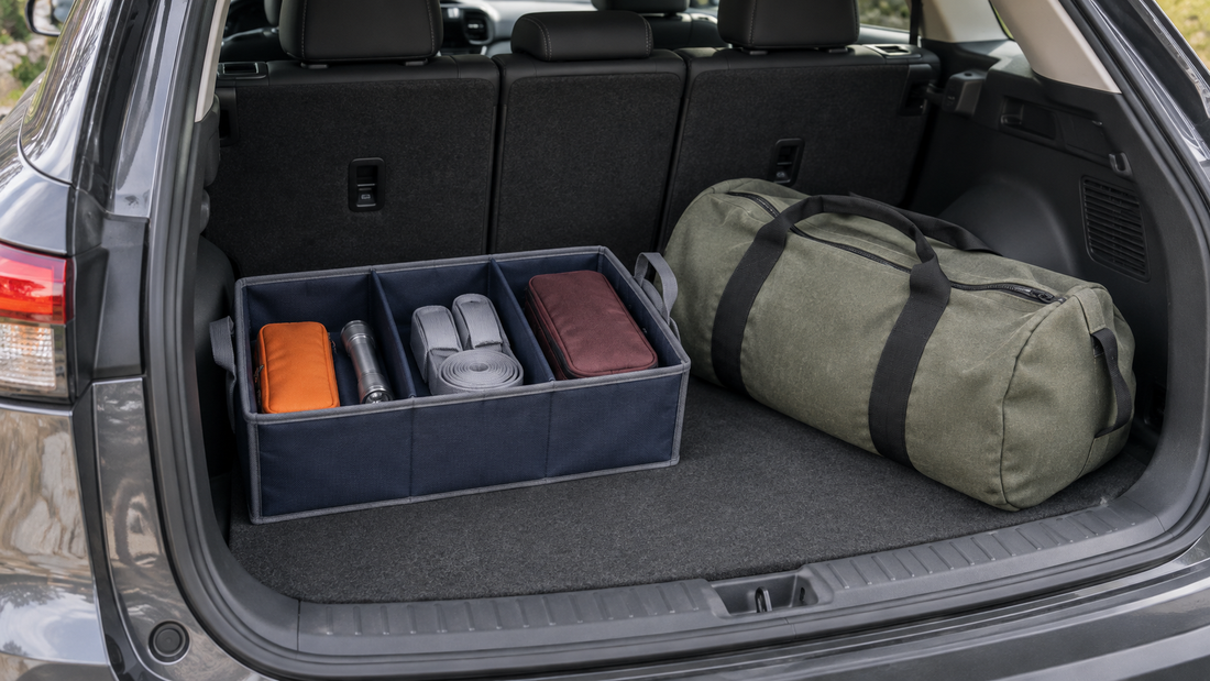 A navy divided trunk organizer holds small accessories beside a large sage duffel bag resting on the open cargo floor.