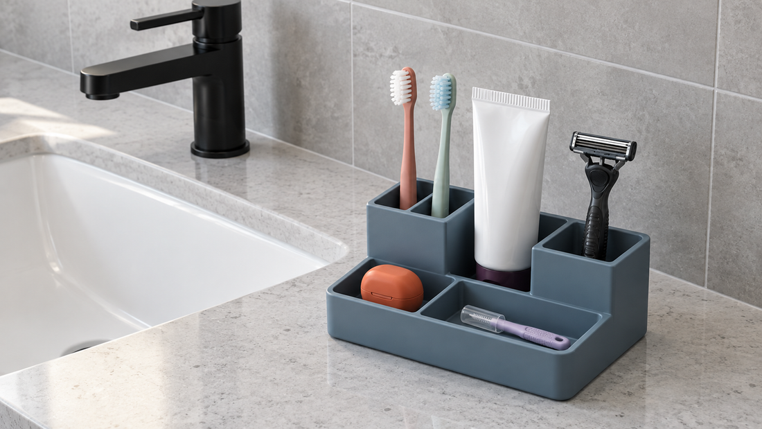 : A blue divided organizer holds toothbrushes, toothpaste, a razor, floss, and a capped interdental brush in separate sections beside a bathroom sink.