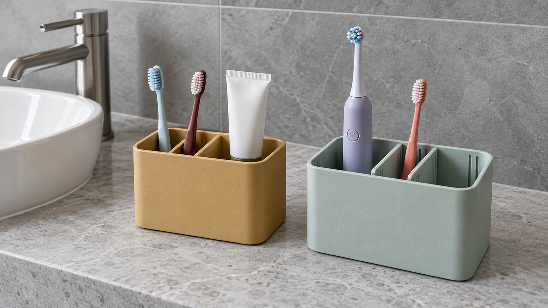 An ochre organizer has fixed compartments, while a seafoam organizer uses repositionable dividers to separate electric and manual toothbrushes on a bathroom counter.