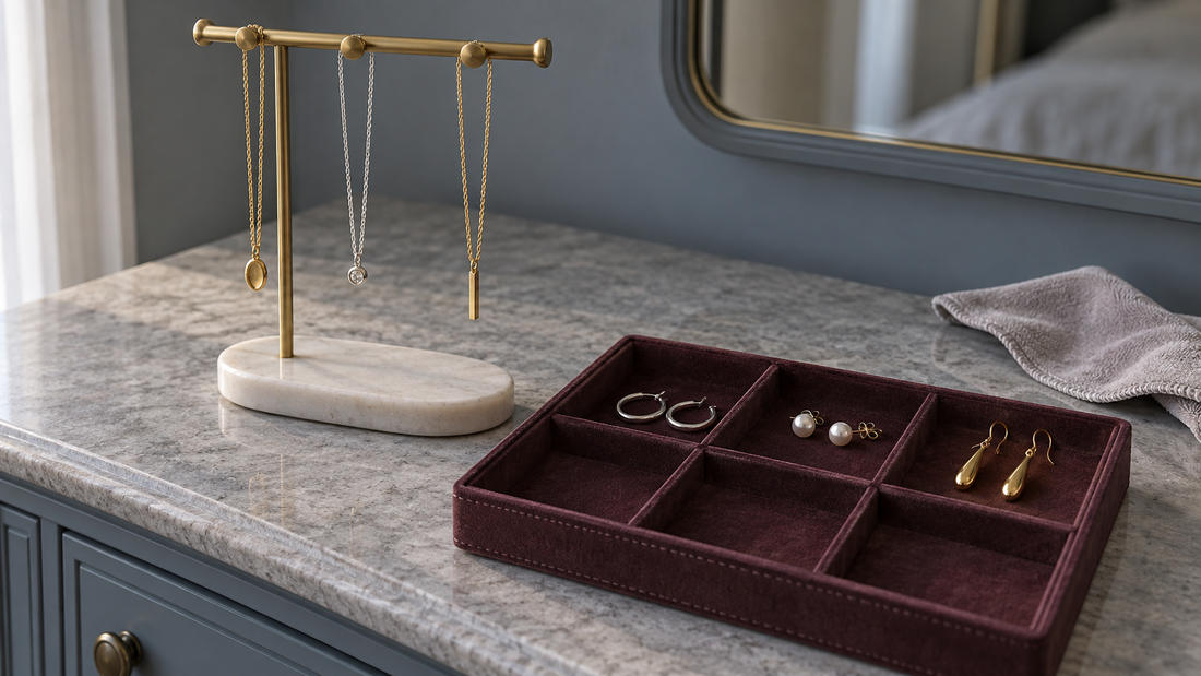 Necklaces hang separately on a brass stand beside a burgundy divided tray holding paired hoops, pearl studs, and drop earrings.