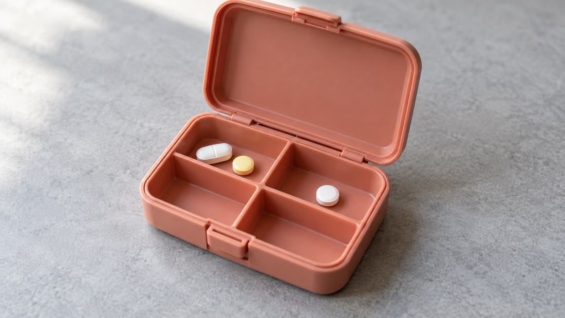 An open coral travel pill organizer holds tablets below the compartment rims, leaving the lid, hinge, and front clasp unobstructed.