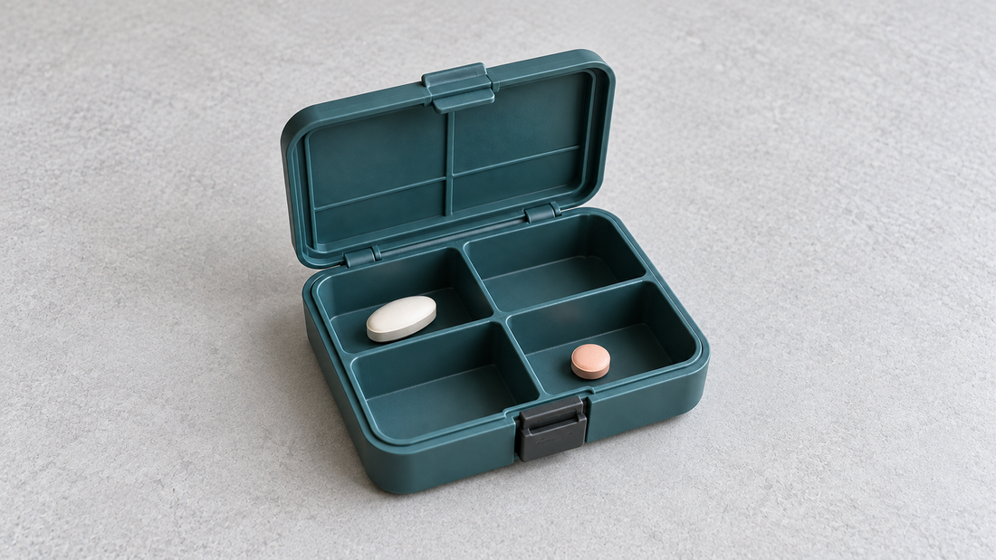 A fully visible open teal travel pill organizer shows its ribbed lid, front clasp, and tablets below the compartment rims.